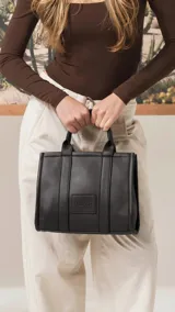 Cartera estructurada de tamaño mediano, confeccionada en símil cuero color negro. Presenta doble asa de mano, correa larga ajustable y desmontable, y un bolsillo trasero con cierre. El compartimento principal cuenta con cierre, división interna y bolsillos organizadores.