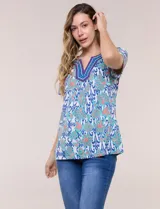 Blusa de manga corta con escote en V y pechera bordada. Presenta un estampado multicolor sobre base blanca, con pliegues frontales y aberturas laterales en el ruedo.