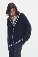 Cardigan de punto negro con diseño estilo varsity, escote en V y cierre frontal de botones. Presenta líneas blancas en contraste a lo largo de la botonera, el escote, los puños y el ruedo.