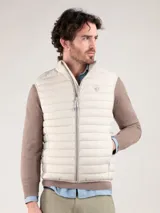 Chaleco acolchado de hombre en color beige, con cuello alto, cierre frontal de cremallera y bolsillos laterales. Presenta diseño capitoné horizontal y detalle de logo engomado en el pecho.