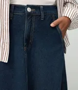 Pollera midi de corte evasé confeccionada en denim de algodón. Presenta un diseño clásico con trabillas en la cintura, cierre frontal con botón y cremallera, bolsillos funcionales y costuras verticales decorativas que realzan la silueta.