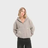 Buzo con capucha y cierre frontal completo, confeccionado en felpa suave color gris. Presenta diseño de corte holgado, bolsillos tipo canguro y detalles estampados minimalistas en el frente.