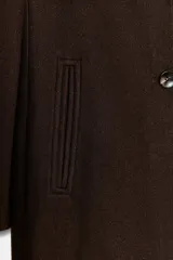 Abrigo de paño color beige con cuello solapa, manga larga con hombreras y cierre frontal con botones. Presenta bolsillos delanteros de doble vivo y abertura en la espalda.