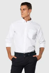 Camisa Oxford lisa de color celeste, con cuello abotonado, manga larga, cierre frontal de botones y un bolsillo aplicado en el pecho con detalle bordado.