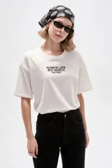 Remera de algodón blanca de manga corta, con cuello redondo y diseño holgado. Cuenta con estampado tipográfico negro en el pecho con la frase 'ALWAYS LATE BUT WORTH THE WAIT'.
