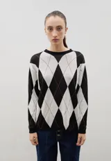 Buzo de punto con diseño de rombos en blanco y negro, con detalles de líneas finas en color naranja. Presenta cuello redondo, mangas largas y puños acanalados.