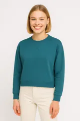 Buzo de cuello redondo en color verde azulado, con detalle de costura en forma de X en el pecho, mangas largas con puños elásticos y ruedo recto acanalado.