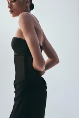 Vestido midi negro de escote palabra de honor, con diseño combinado de paneles de distintos acabados y detalle drapeado en la zona frontal y de la cintura. Cuenta con cierre lateral de cremallera oculta.