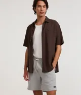Bermuda de sarga color beige, de corte recto, con cintura elástica y cordón ajustable. Cuenta con bolsillos laterales y un discreto parche con logo aplicado en el dobladillo inferior.