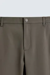 Pantalón de corte slim fit confeccionado en tejido elástico, con cintura elástica, cierre frontal con cremallera y botón, bolsillos laterales y bolsillos traseros de vivo.