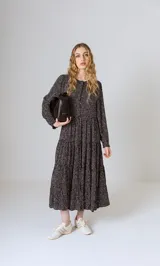 Vestido midi negro con estampado de lunares blancos, corte amplio, mangas largas con puños elásticos y cuello redondo con abertura y botón.