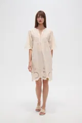 Vestido corto color crema, con escote en V y mangas 3/4. Presenta detalles de bordado inglés (broderie) en el canesú superior y en el ruedo inferior.