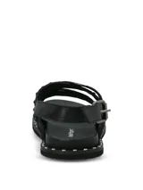 Sandalias negras de cuero con diseño de tiras cruzadas, decoradas con tachas metálicas. Poseen ajuste mediante hebilla lateral y suela de goma con detalle de tachas en el borde.