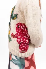 Sweater de lana merino color beige, tejido a mano con diseño holgado, cuello redondo y bordados artesanales de ranas y detalles coloridos.