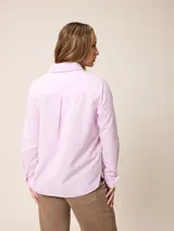 Camisa de manga larga con cuello clásico y cierre frontal de botones, confeccionada en tela de algodón con diseño de rayas verticales finas en color rosado y blanco. Presenta un bolsillo frontal en el pecho con detalle de etiqueta pequeña.