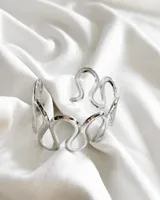 Pulsera rígida plateada con diseño abstracto de líneas onduladas.