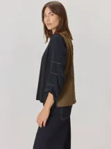 Chaleco de diseño original con frente de paño de lana negro y espalda de tejido en tono verde oliva. Presenta un maxi bordado artístico en la espalda que representa una hoja de ciprés calvo.