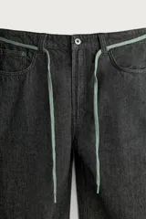 Jeans wide fit de denim negro, con costuras y detalles en color verde claro, bolsillos laterales y traseros, y cintura ajustable con cordón integrado.