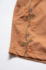Short de baño color arcilla con bordado de enredadera en la pierna, cintura elástica con cordón ajustable, bolsillos laterales y bolsillo trasero con cierre.