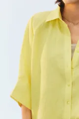 Camisa oversize blanca de lino, con corte cuadrado, mangas raglán cortas con puños anchos, aberturas laterales y cierre frontal de botones.