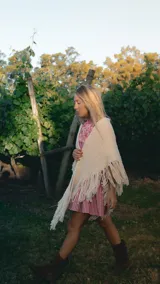 Ruana tejida a mano en forma triangular, color crudo, confeccionada en lana merino con detalle de flecos largos en los bordes.