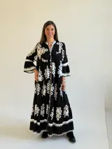 Vestido largo negro con estampado floral blanco, escote en V con cuello mao, cierre frontal de botones y mangas tres cuartos acampanadas.