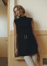 Vestido corto de cuello alto y sin mangas, confeccionado en tejido fluido. Presenta un diseño entallado con cinturón decorativo a la cintura y cierre de cremallera en la parte posterior.