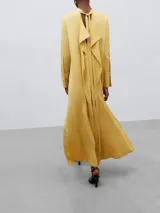 Vestido largo de corte recto y silueta fluida, confeccionado en viscosa. Presenta cuello mao con cierre de botón oculto, mangas largas con puños abotonados y aberturas laterales en el ruedo.
