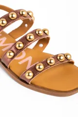 Sandalias planas Lemon de cuero color bronce, con tres tiras frontales adornadas con tachas semiesféricas doradas y cierre de hebilla ajustable en el talón.