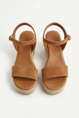 Sandalia de gamuza color negro con plataforma de yute trenzado, tira ancha en la parte delantera y tira ajustable al tobillo con hebilla metálica dorada.