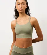 Top deportivo de microfibra en color verde oliva, con diseño de corte largo, breteles finos y detalle de friso contrastante en tono beige. Incluye copas para mayor sujeción.
