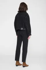 Chaqueta de denim negra de corte relajado, con cuello clásico, cierre frontal con botones metálicos y bolsillos con solapa en el pecho.