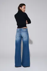 Pantalón de jean de tiro medio y pierna ancha, con lavado claro y zonas desgastadas.