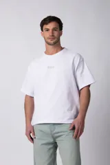 Remera de corte boxy y fit cuadrado, confeccionada en algodón grueso. Presenta un diseño minimalista con un pequeño logo circular en el pecho y una estampa de gran tamaño en la espalda con la frase 'Designed in South America, Worldwide Clothes'.