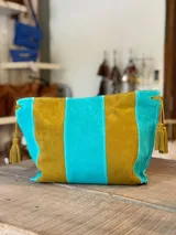 Cartera tipo sobre de cuero con diseño de rayas verticales en tonos verde menta y marrón tostado. Cuenta con detalles de borlas colgantes en los laterales.