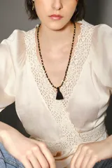 Collar largo con diseño de cuentas doradas intercaladas en un cordón negro, finalizado con una borla negra central.