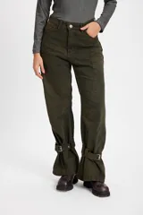 Jean tipo baggy de pierna ancha y recta, color marrón oscuro. Presenta detalles de costuras decorativas, bolsillos laterales redondeados y bolsillos traseros grandes. Incluye tiras ajustables con hebillas metálicas en los tobillos para un efecto fruncido.