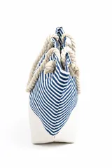 Bolso tipo tote de playa, con diseño de rayas horizontales en color gris y base blanca. Cuenta con asas de soga gruesa en color crudo con nudos decorativos.