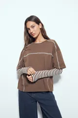 Remera de manga corta con silueta relajada y costuras a la vista en color blanco que contrastan sobre el tejido negro. Presenta un diseño moderno con terminaciones destacadas.