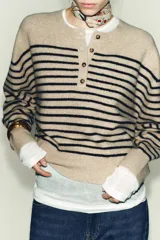 Jersey de punto de manga larga con cuello redondo y cierre frontal parcial con botones. Presenta un diseño a rayas horizontales en contraste sobre fondo beige.
