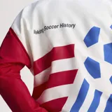 Campera deportiva Adidas de tejido técnico con cierre frontal y cuello alto. Presenta un diseño estampado con motivos de la Copa del Mundo USA 94, combinando colores blanco, azul y rojo. Cuenta con bolsillos laterales con cremallera y puños elásticos.