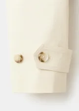 Chaqueta de algodón elastizado color beige, con cuello alto, cierre frontal de botonadura simple, mangas largas y cinturón ajustable del mismo tejido.