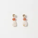 Caravanas colgantes con base metálica dorada de forma irregular, una cuenta de piedra color terracota y un dije inferior de resina con efecto marmolado en tonos crema y blanco.