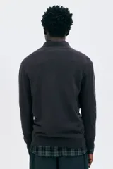 Buzo de punto fino color marrón oscuro, con cuello alto acanalado y medio cierre frontal. Presenta remates acanalados en puños y bajo.