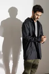 Campera impermeable verde con capucha, cierre frontal con botones a presión, bolsillos laterales con solapa y puños ajustables.