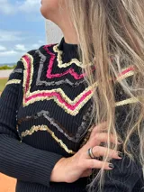 Buzo negro de tejido de punto con cuello alto y mangas largas. Presenta un diseño de líneas zigzagueantes en el frente y los hombros, decorado con lentejuelas doradas, rosas y grises.