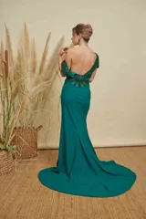 Vestido largo de fiesta color verde esmeralda, con escote ilusión, mangas cortas con detalles de pedrería y bordados, y cintura marcada con aplique de pedrería. Presenta una falda con caída fluida y pequeña cola.