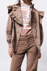 Campera de pana color blanco, de corte oversize, con cuello alto, cierre frontal de botones y volados decorativos en los hombros y cuello.
