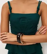 Blusa verde oscuro de viscolino con tirantes dobles ajustables mediante nudos. Presenta un corpiño estructurado con un detalle de flor en relieve en la parte delantera y smock en la espalda para un mejor ajuste. La prenda tiene un bajo peplum.