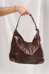 Cartera tipo hobo de cuero sintético marrón oscuro, con diseño slouchy y costura central vertical. Posee asa corta integrada al cuerpo del bolso.